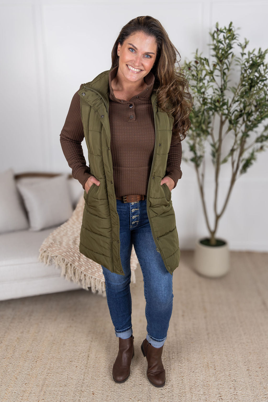 Woman wearing Whitley Waffle Snap Pullover in brown waffle knit with kangaroo pocket and snap neckline. Paired with the  Harlow vest in army green.