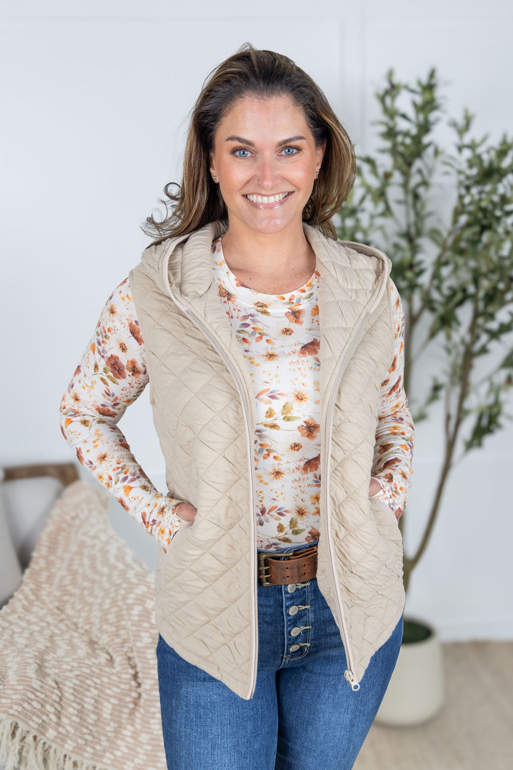 Woman wearing beige quilted hooded vest with zipper and pockets.
