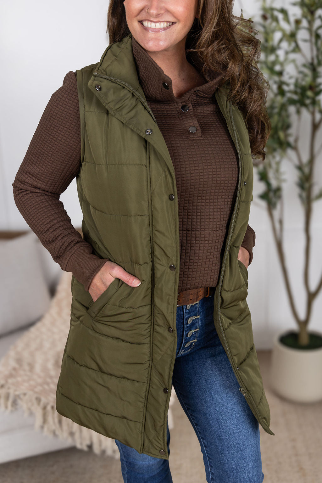 Woman wearing Whitley Waffle Snap Pullover in brown waffle knit with kangaroo pocket and snap neckline. Paired with the  Harlow vest in army green.
