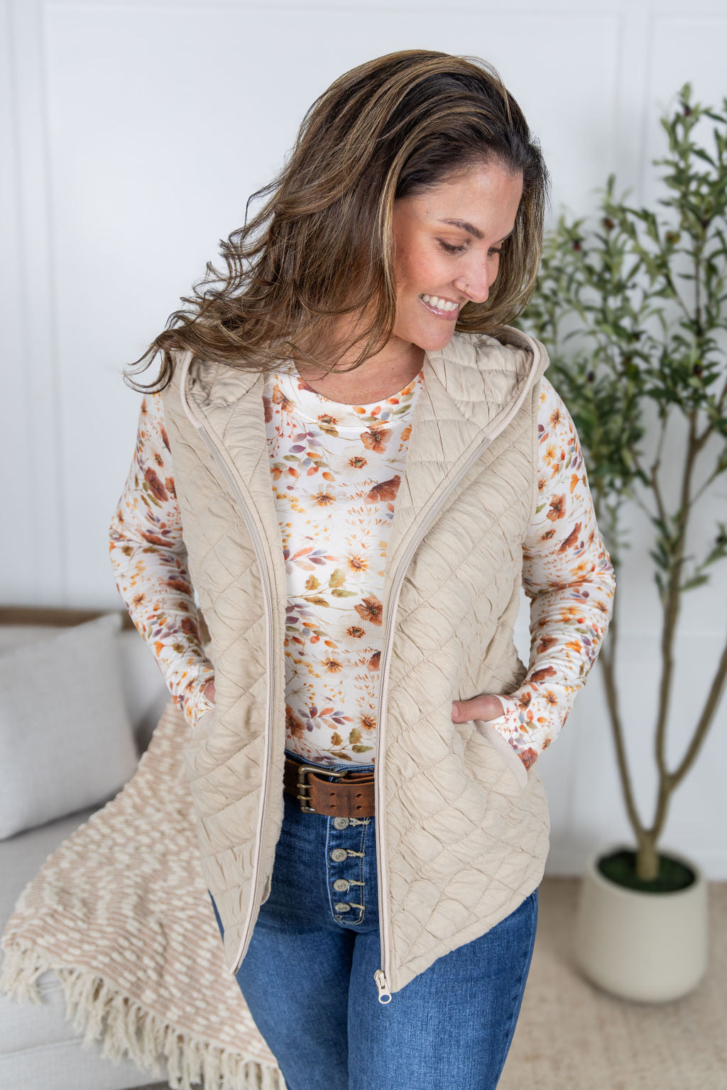 Woman wearing beige quilted hooded vest with zipper and pockets.