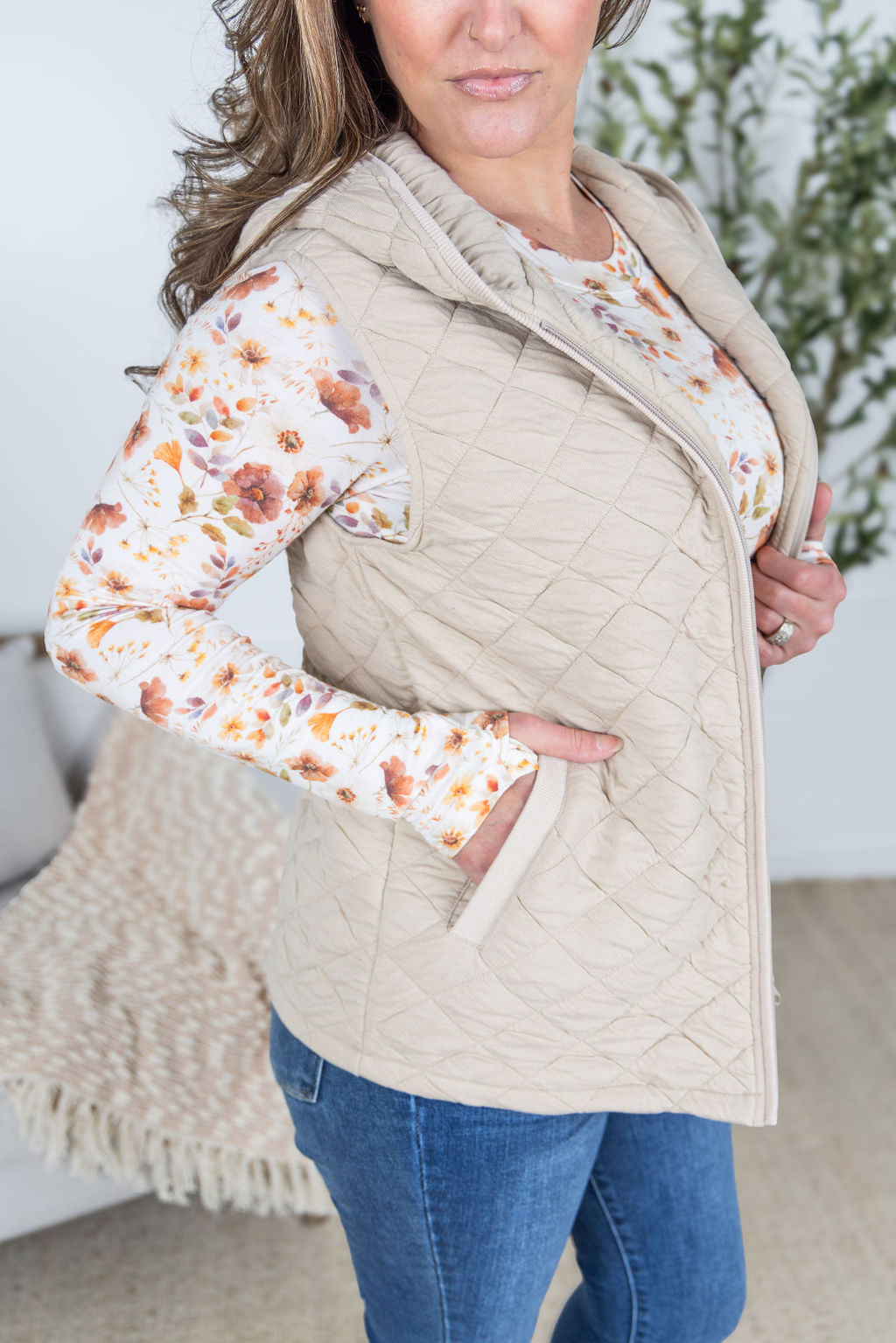Woman wearing beige quilted hooded vest with zipper and pockets.