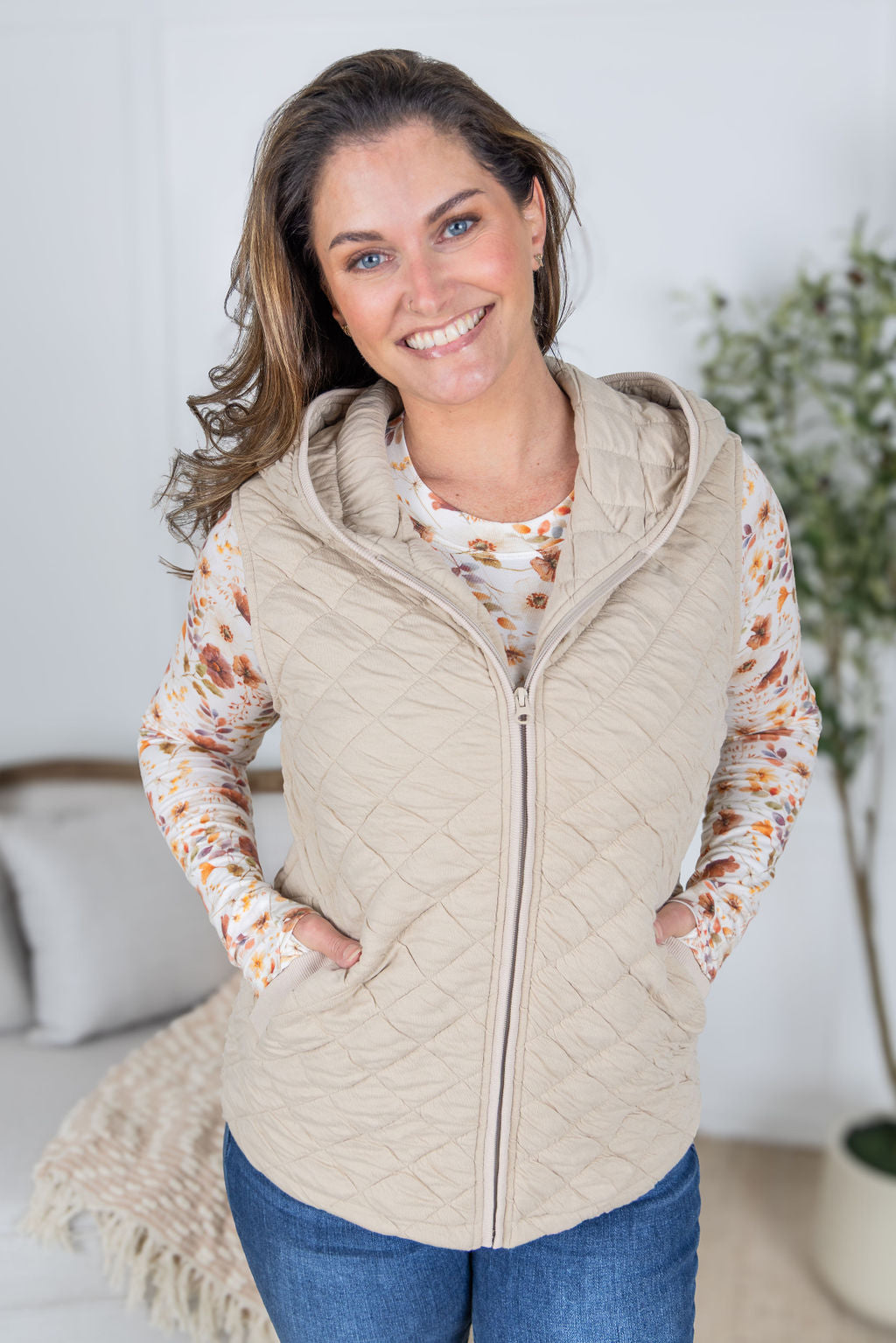 Woman wearing beige quilted hooded vest with zipper and pockets.