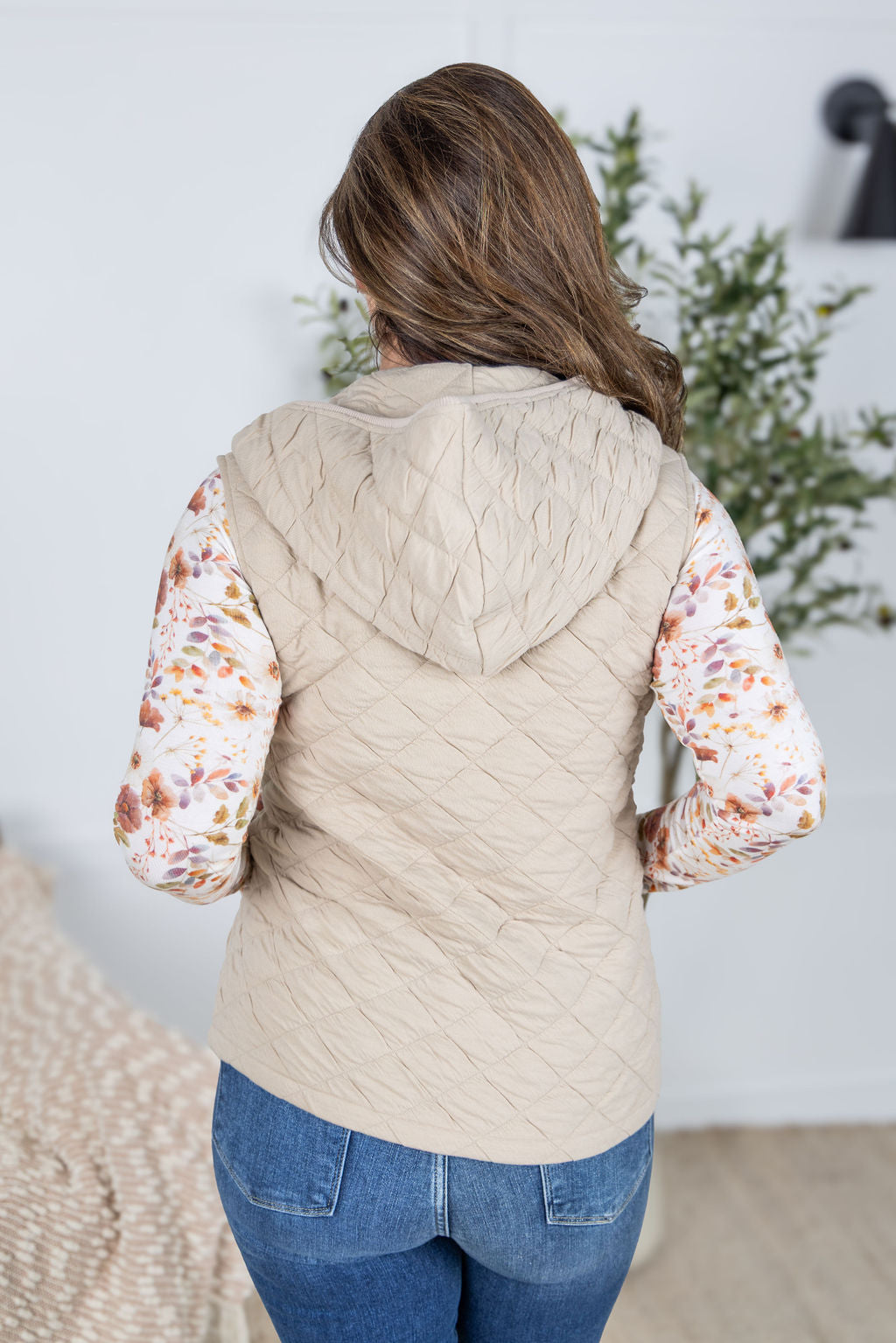 Woman wearing beige quilted hooded vest with zipper and pockets.