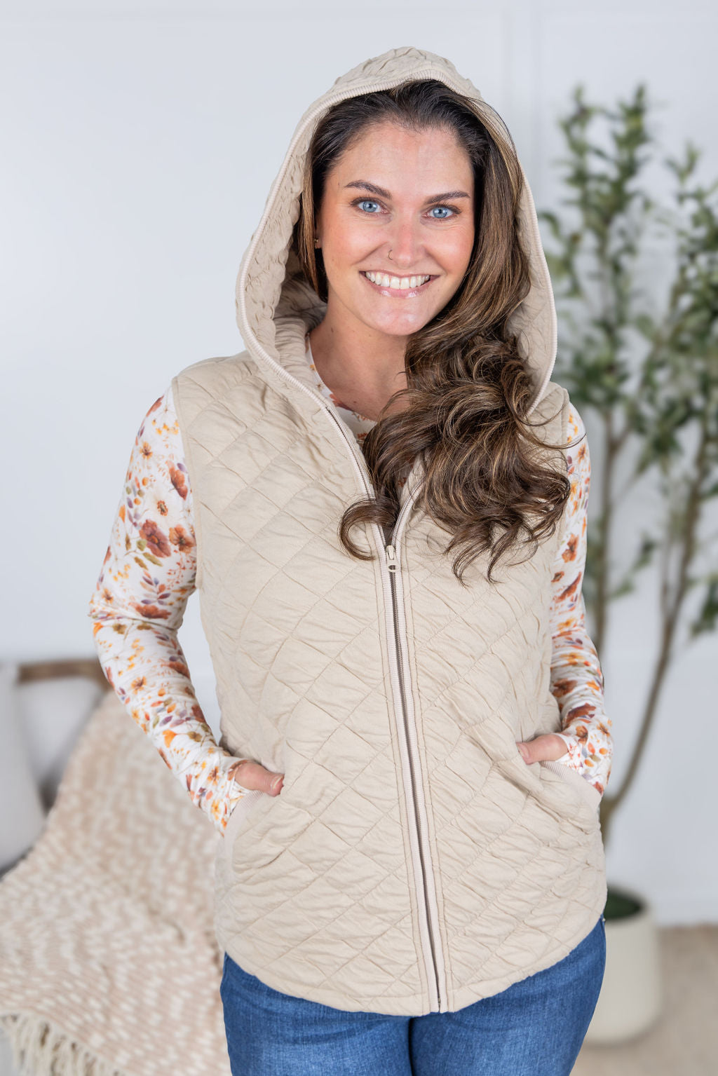 Woman wearing beige quilted hooded vest with zipper and pockets.