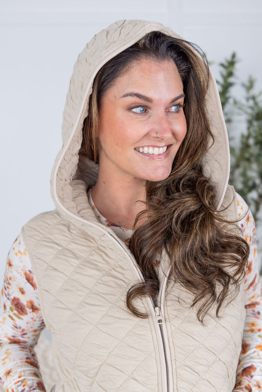 Woman wearing beige quilted hooded vest with zipper and pockets.