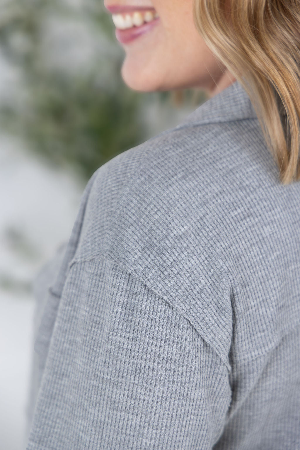 Woman wearing grey waffle knit button top with long sleeves and chest pockets.