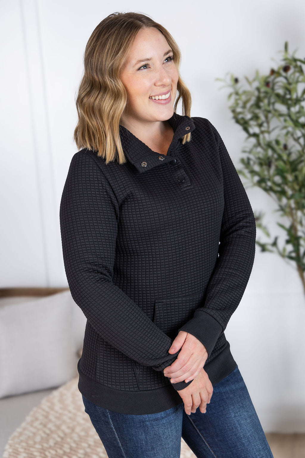 Woman wearing black Whitley Waffle Snap Pullover with waffle knit, snap buttons, and kangaroo pocket.