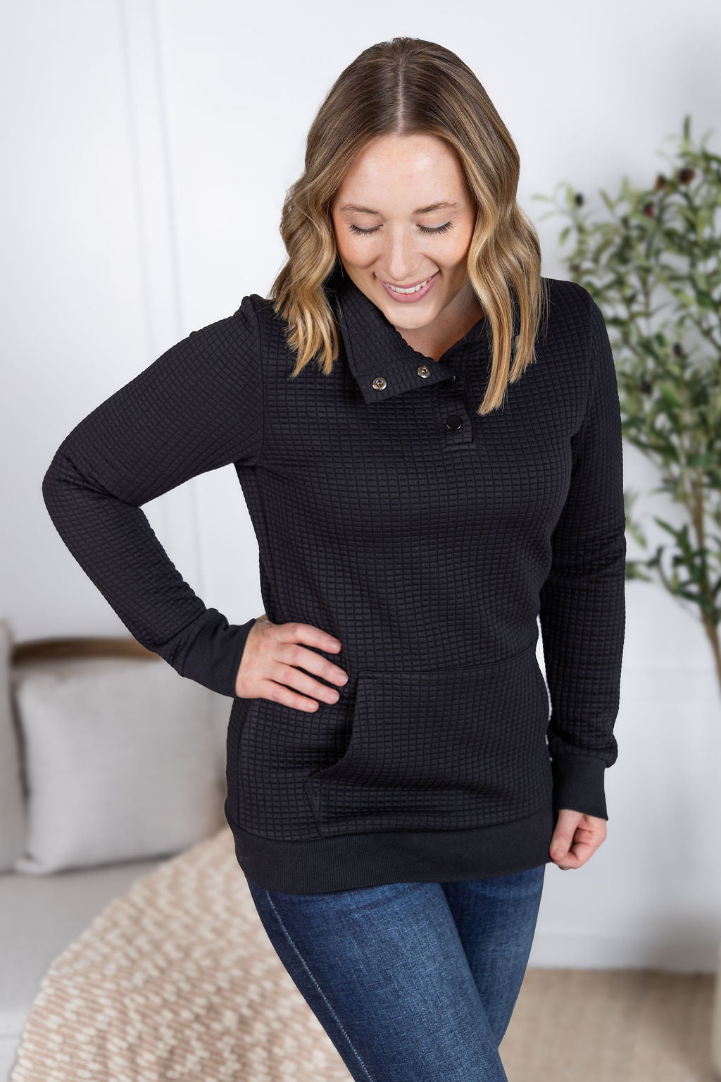 Woman wearing black Whitley Waffle Snap Pullover with waffle knit, snap buttons, and kangaroo pocket.