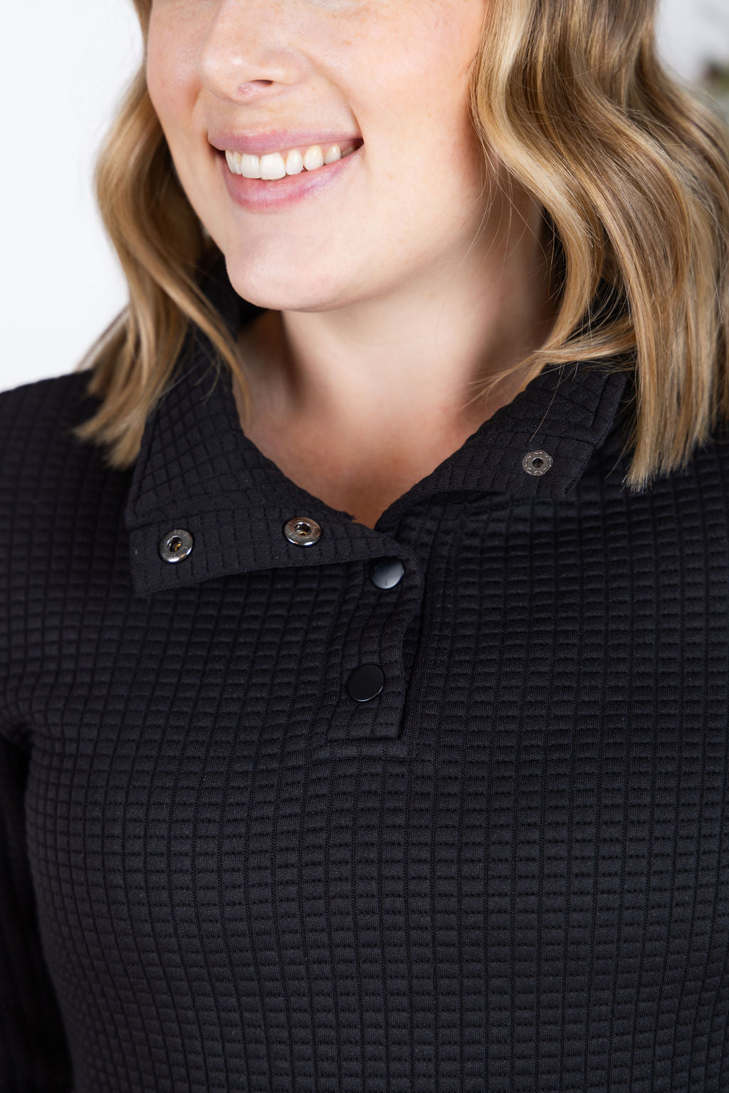 Woman wearing black Whitley Waffle Snap Pullover with waffle knit, snap buttons, and kangaroo pocket.