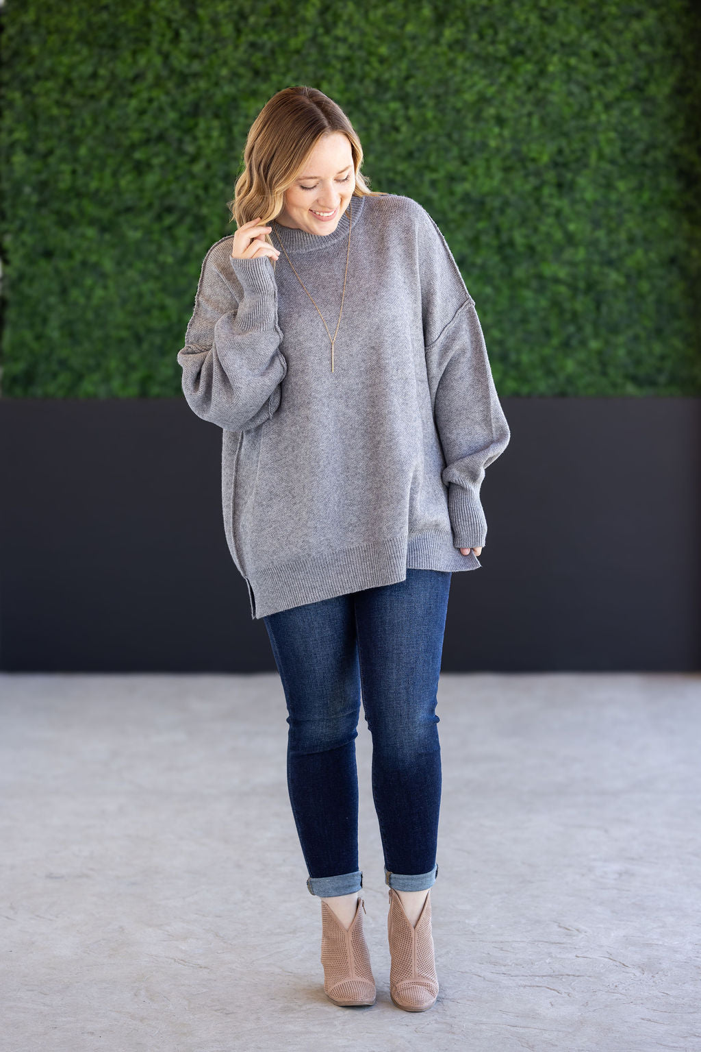 Woman wearing the Aurora Cozy Sweater in gray with mock neck, seam detail, and side slits.