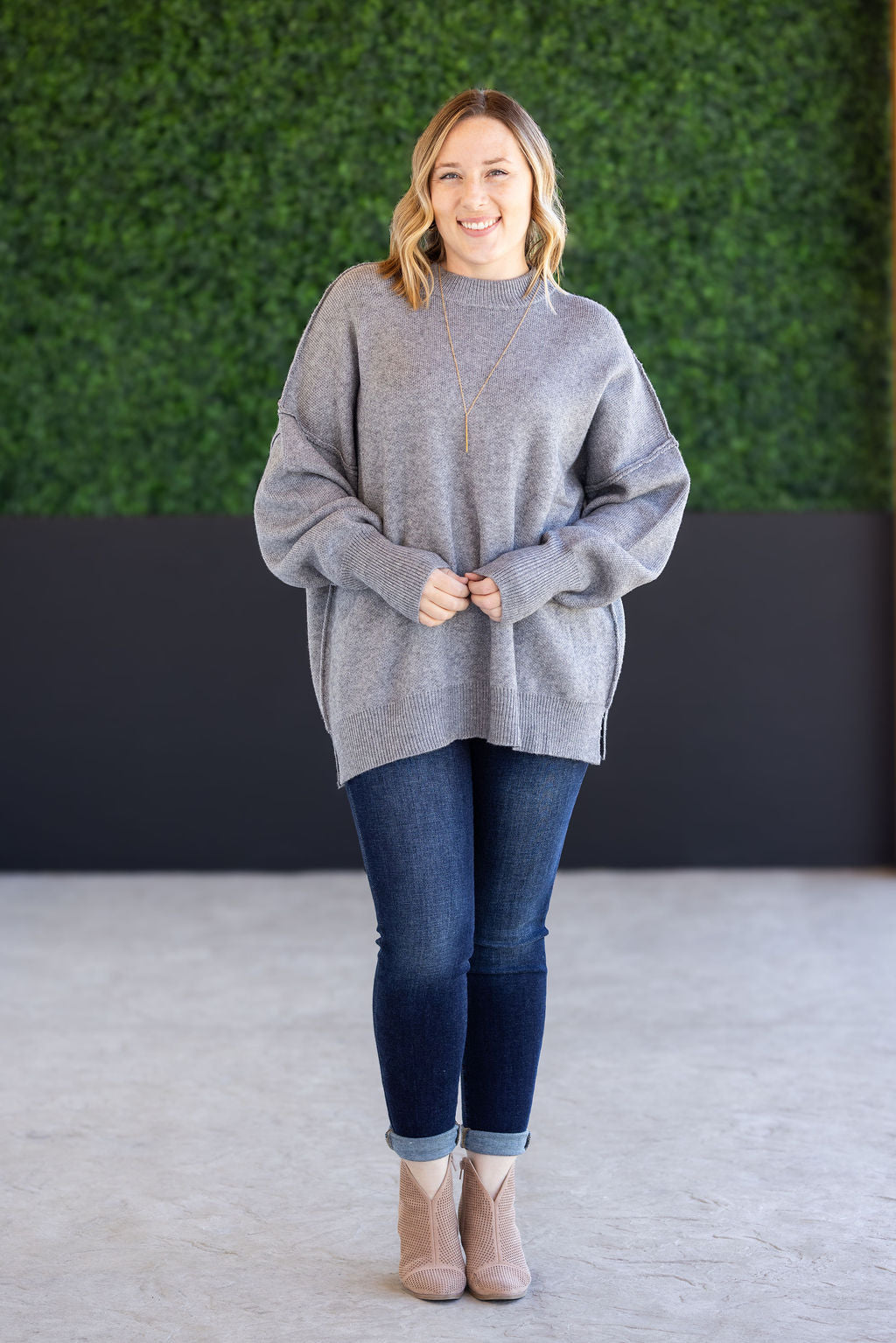 Woman wearing the Aurora Cozy Sweater in gray with mock neck, seam detail, and side slits.
