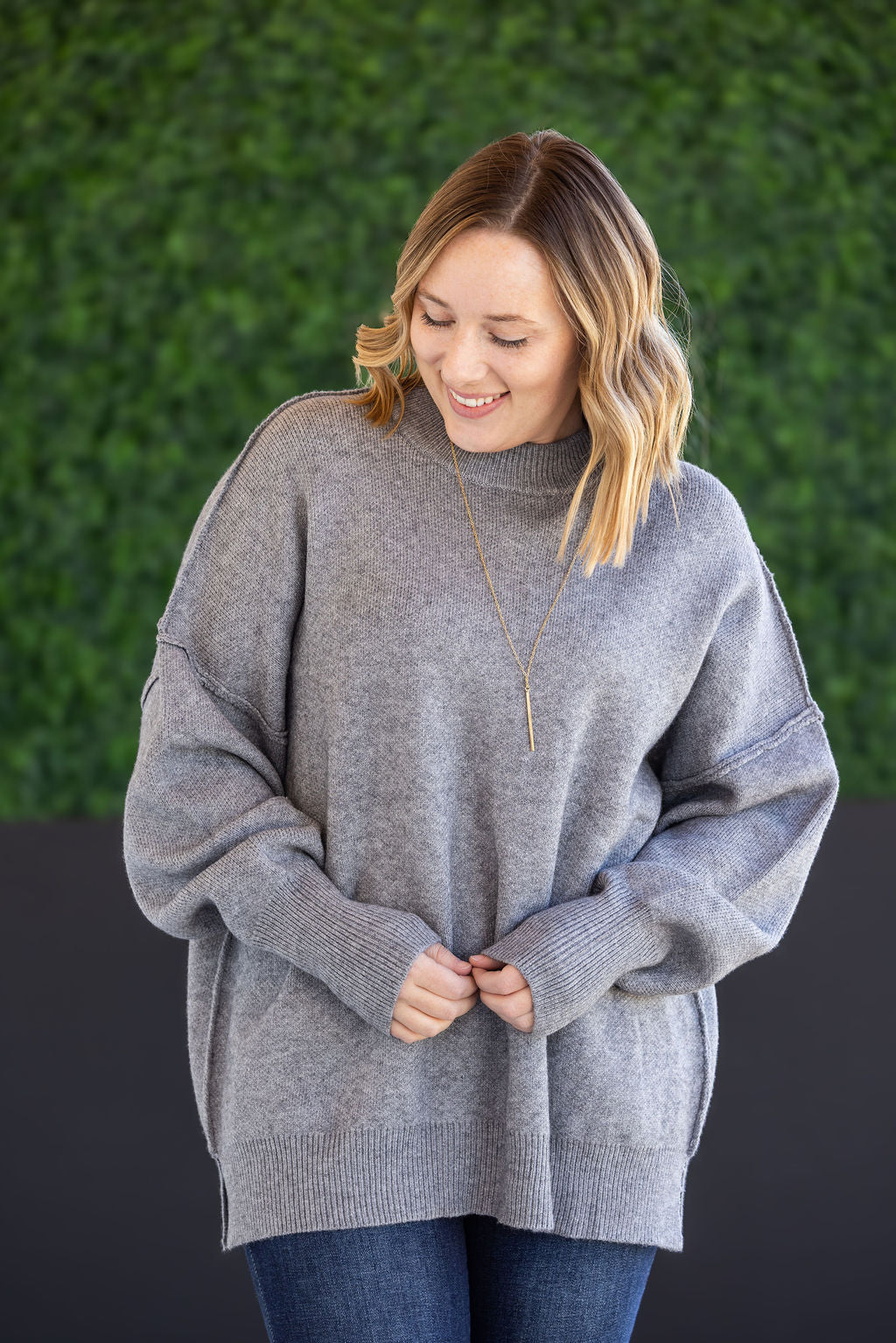 Woman wearing the Aurora Cozy Sweater in gray with mock neck, seam detail, and side slits.