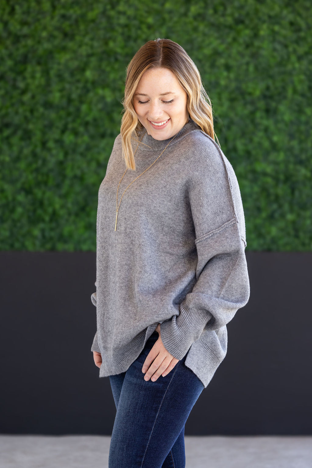 Woman wearing the Aurora Cozy Sweater in gray with mock neck, seam detail, and side slits.