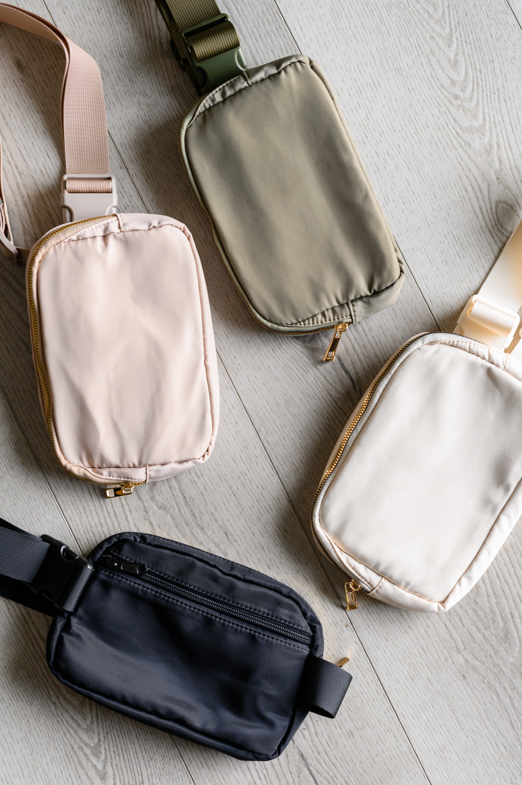 Five different colored fanny packs on a light wooden surface
