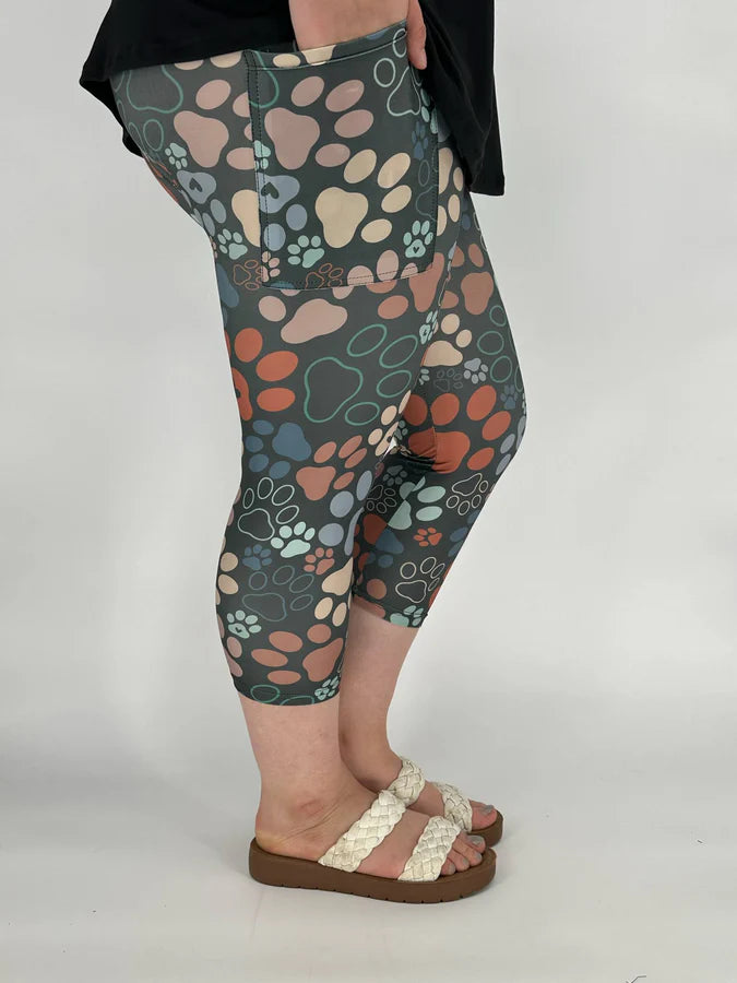 Capri leggings with colorful paw print pattern worn by a person on a plain background