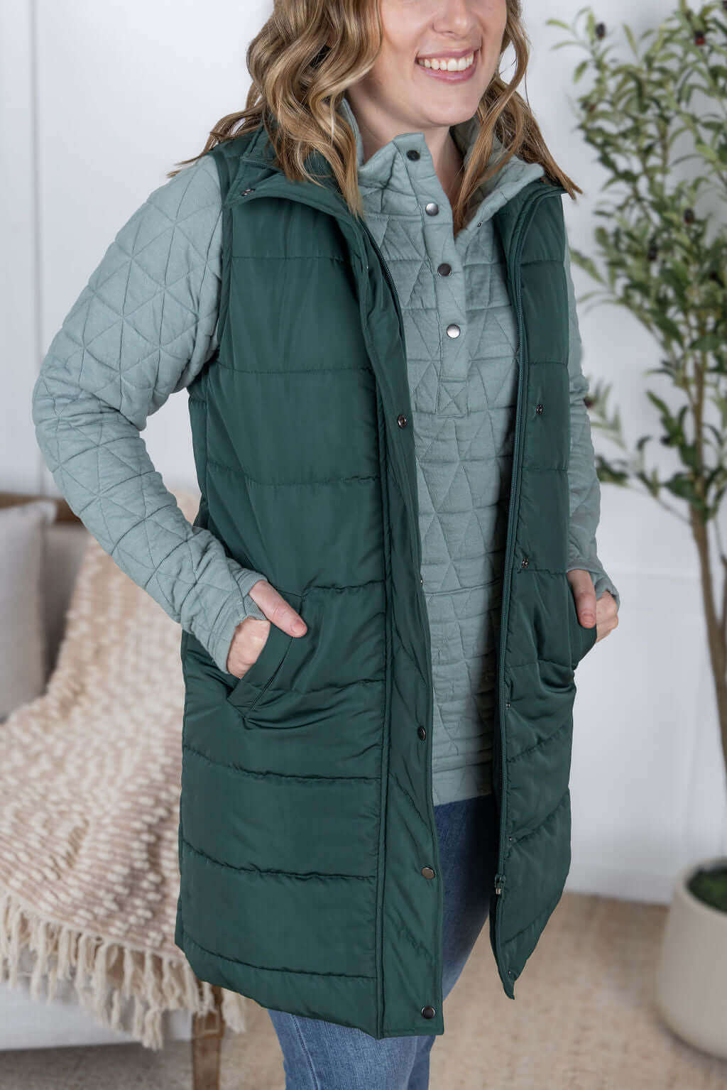Woman wearing a green quilted vest over a light gray pullover, showcasing stylish outerwear for layering.