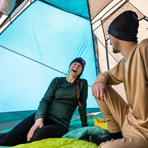 Couple enjoying laughter in a tent, wearing comfortable merino wool clothing for outdoor adventures.