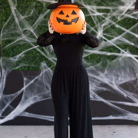 Woman wearing witch hat, with a jack o lantern head, and the Paige Jumpsuit by Michelle Mae
