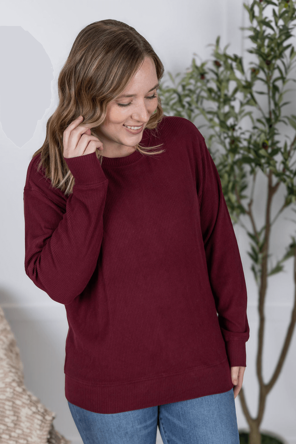 Woman in a cozy maroon top, smiling and posing in a casual indoor setting.