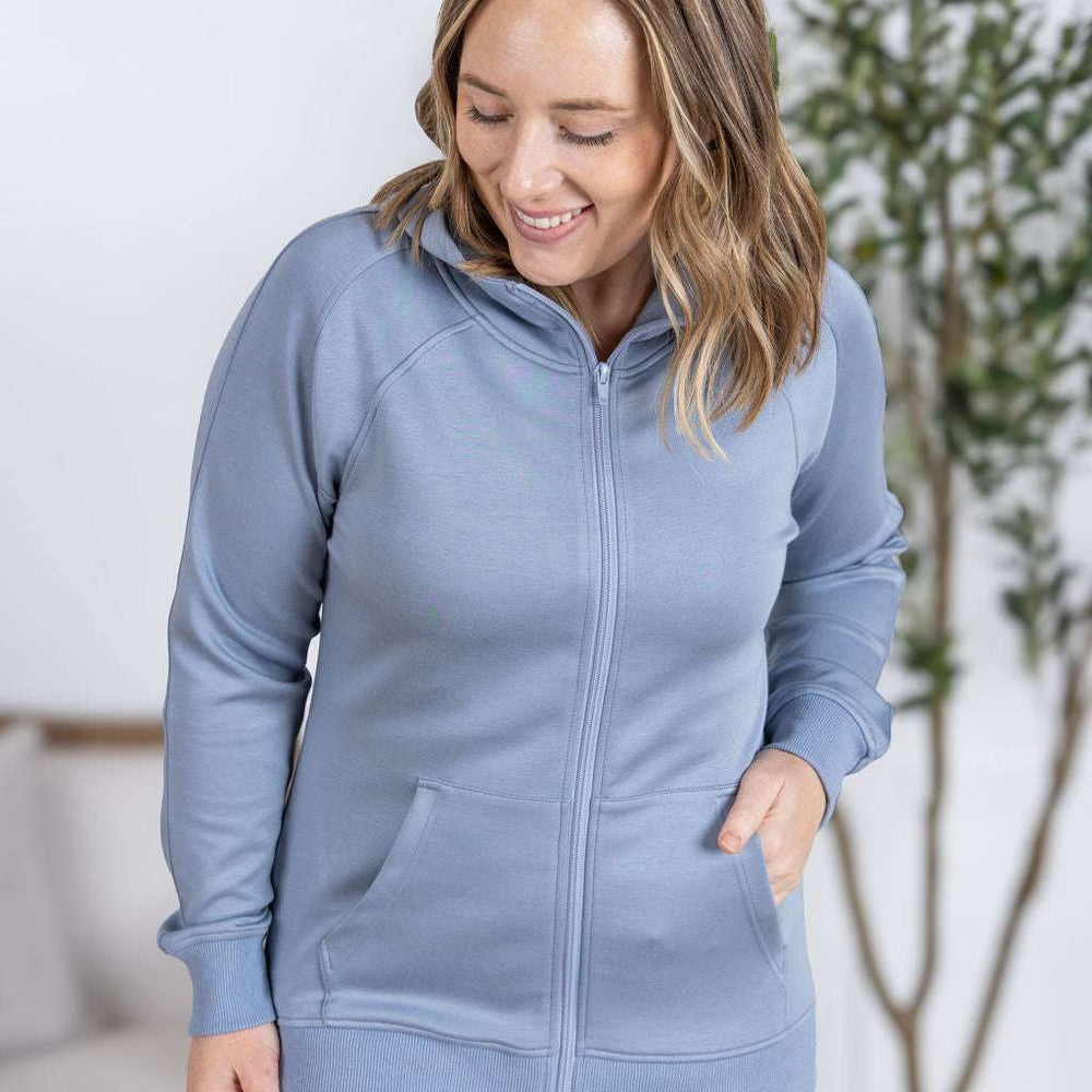 Close-up of a smiling model wearing the Scuba FullZip Hoodie in Dusty Blue, featuring a front zipper closure, cozy hood, and relaxed fit.