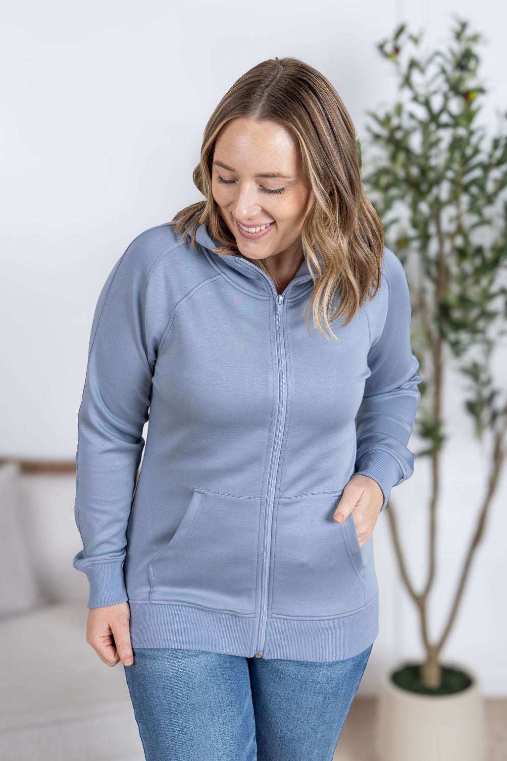 Close-up of a smiling model wearing the Scuba FullZip Hoodie in Dusty Blue, featuring a front zipper closure, cozy hood, and relaxed fit.