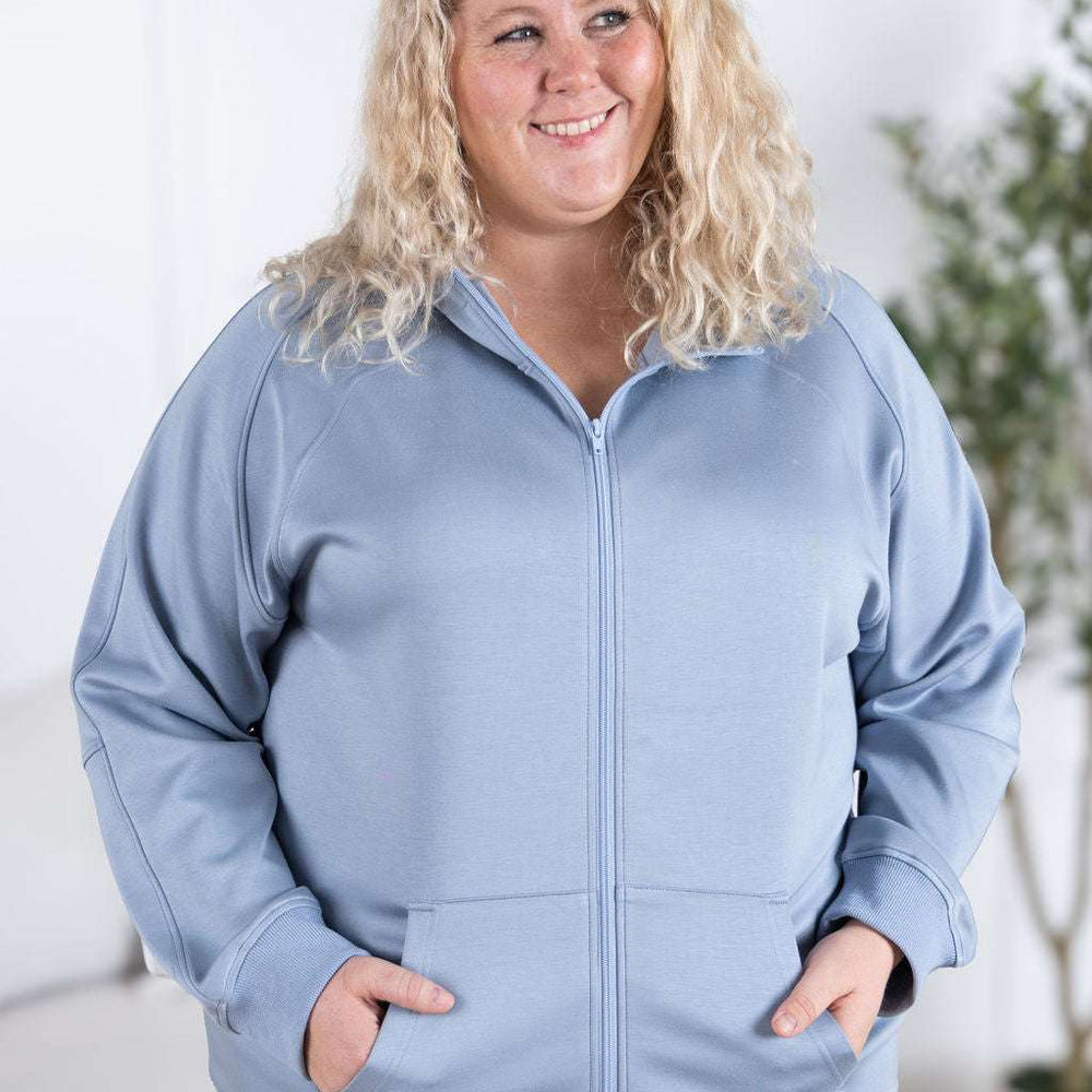 
                  
                    Close-up of a smiling model wearing the Scuba FullZip Hoodie in Dusty Blue, featuring a front zipper closure, cozy hood, and relaxed fit.
                  
                