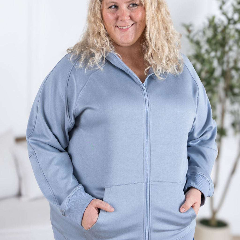 
                  
                    Close-up of a smiling model wearing the Scuba FullZip Hoodie in Dusty Blue, featuring a front zipper closure, cozy hood, and relaxed fit.
                  
                