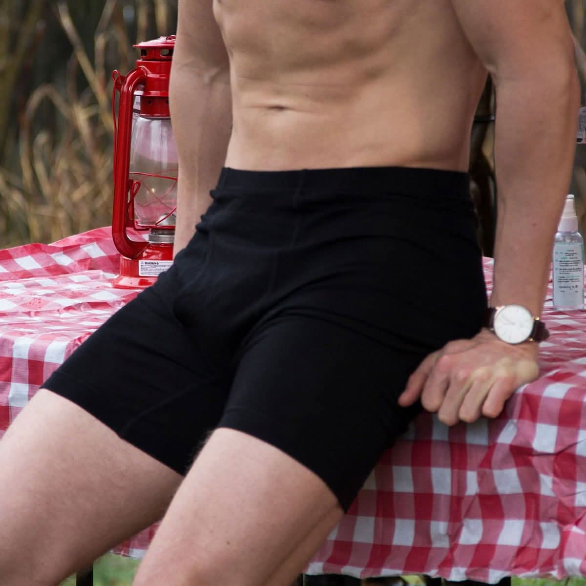 Man wearing black merino wool boxer briefs while sitting at picnic table