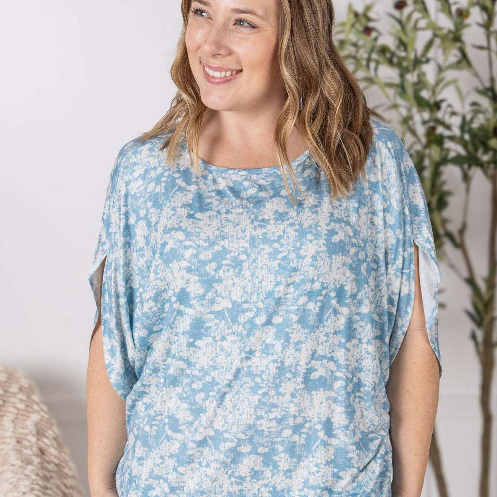 Close-up of a smiling model wearing the Darcy Dolman Top in a soft blue and ivory abstract print, featuring relaxed dolman sleeves and a rounded neckline.