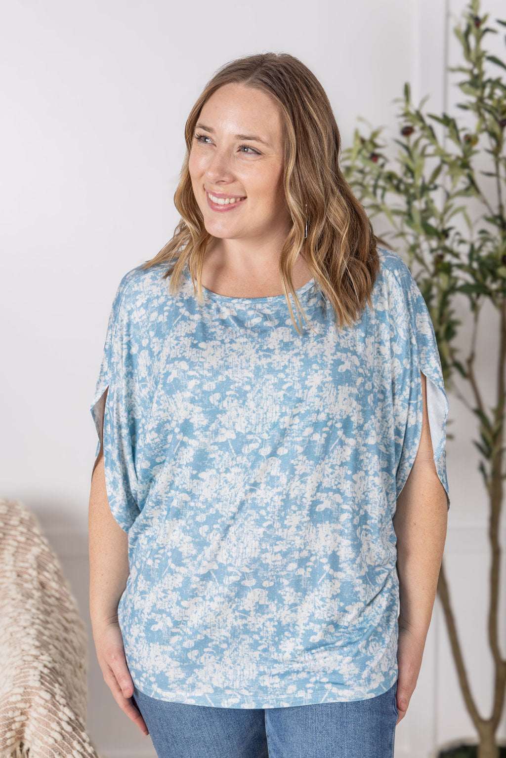 Close-up of a smiling model wearing the Darcy Dolman Top in a soft blue and ivory abstract print, featuring relaxed dolman sleeves and a rounded neckline.