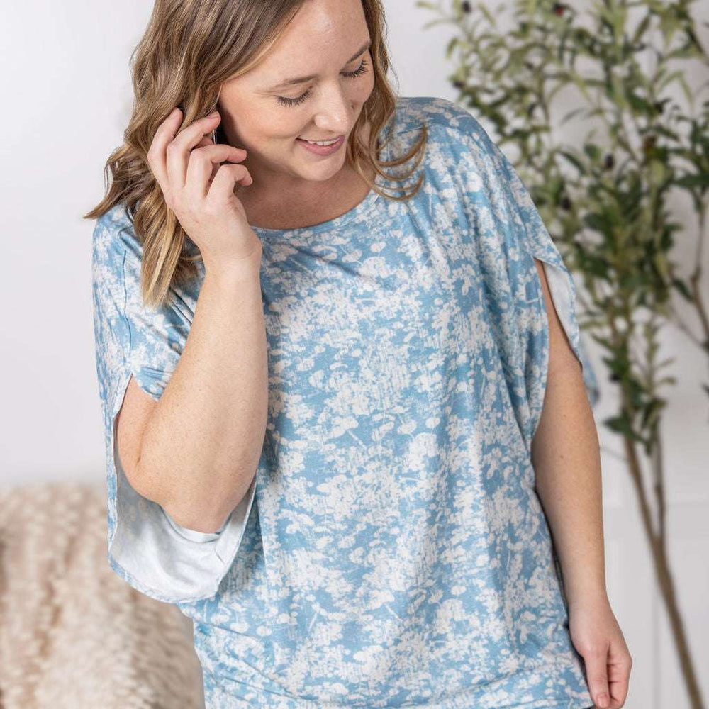 
                  
                    Close-up of a smiling model wearing the Darcy Dolman Top in a soft blue and ivory abstract print, featuring relaxed dolman sleeves and a rounded neckline.
                  
                
