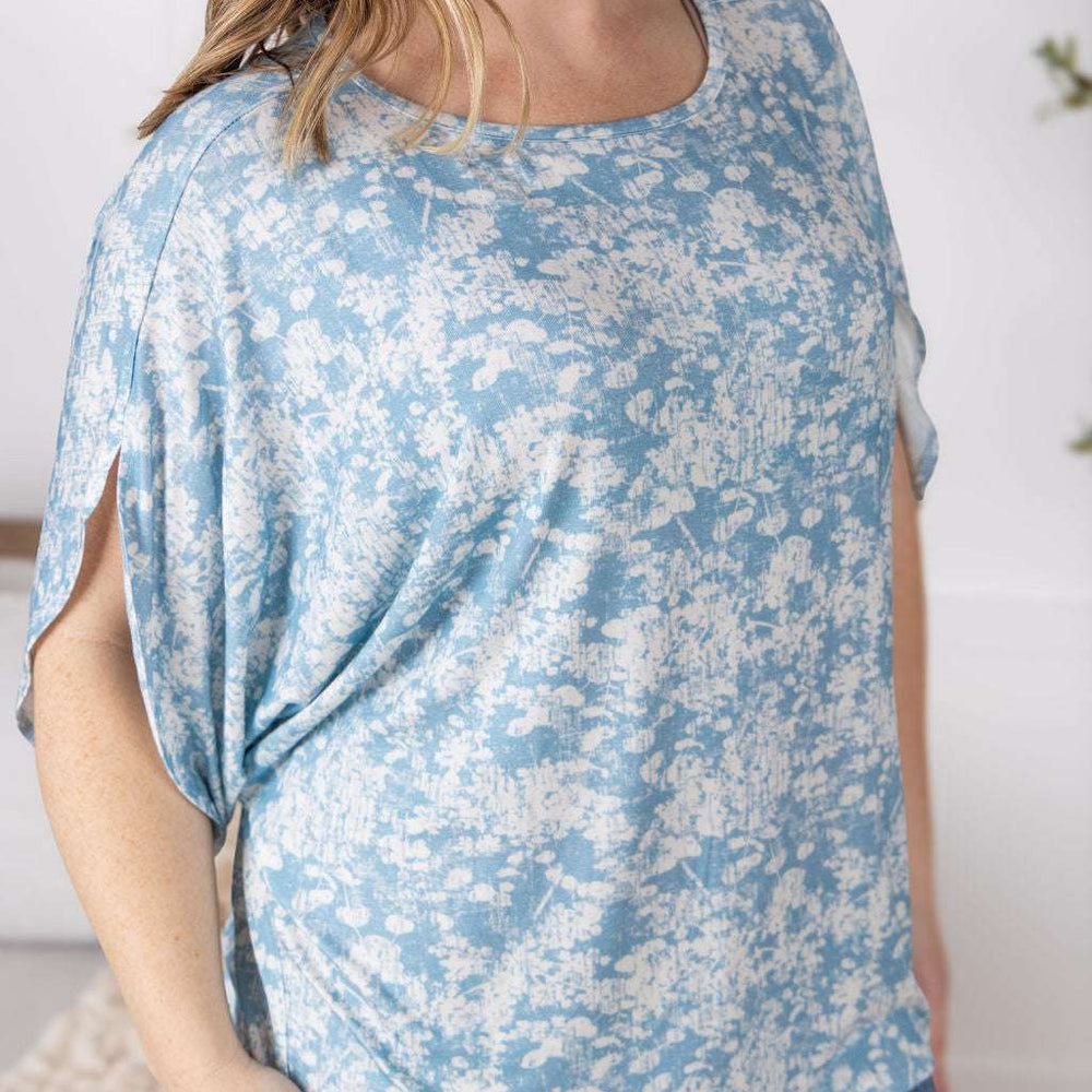 Close-up of a smiling model wearing the Darcy Dolman Top in a soft blue and ivory abstract print, featuring relaxed dolman sleeves and a rounded neckline.