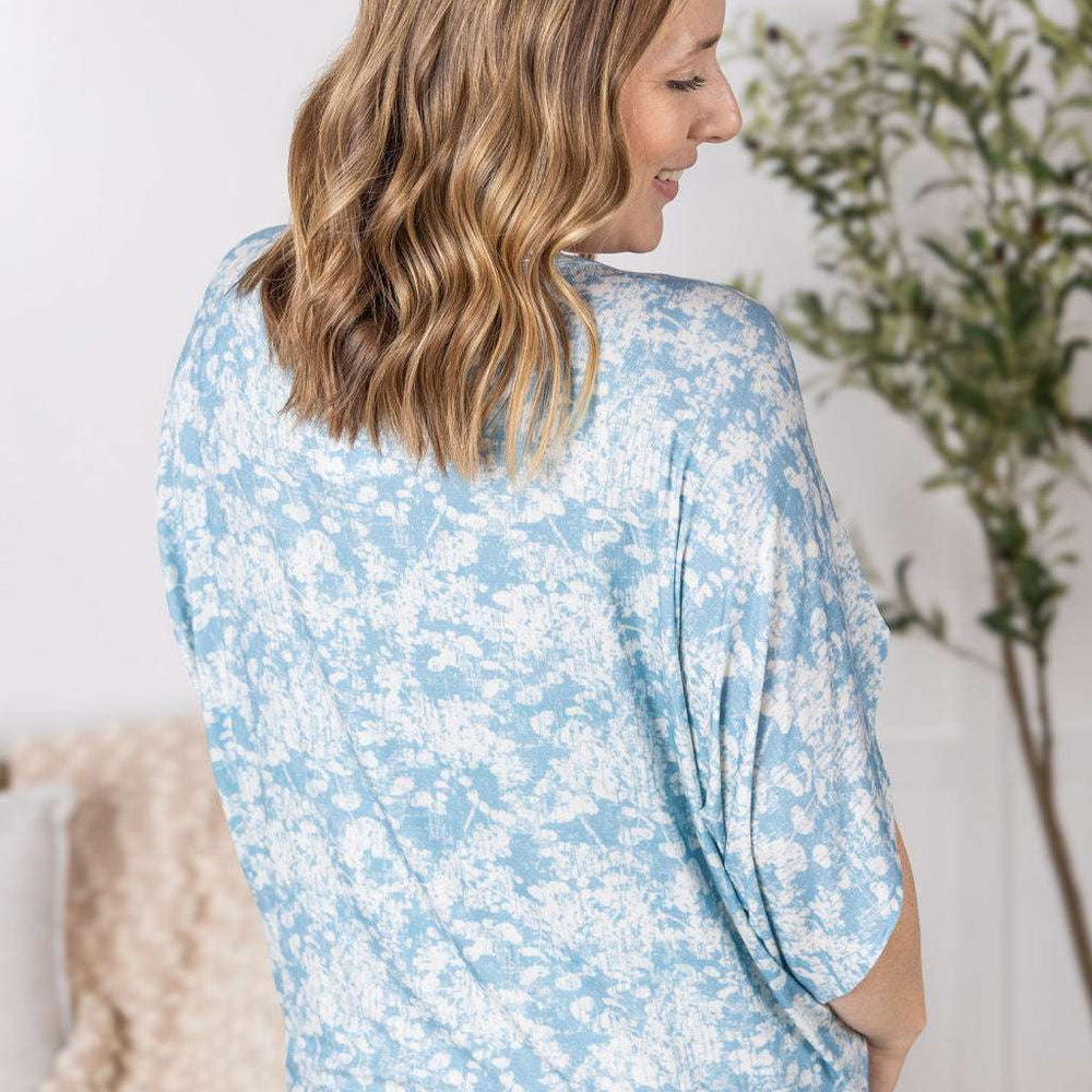 
                  
                    Close-up of a smiling model wearing the Darcy Dolman Top in a soft blue and ivory abstract print, featuring relaxed dolman sleeves and a rounded neckline.
                  
                