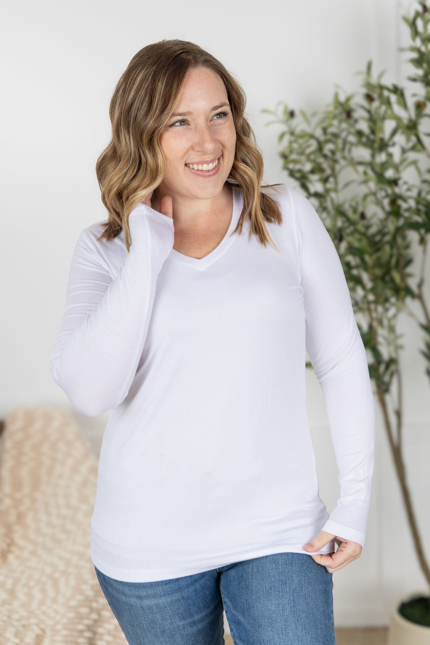 Woman wearing long sleeve v-neck top in classic white with fitted silhouette and flattering v-neckline
