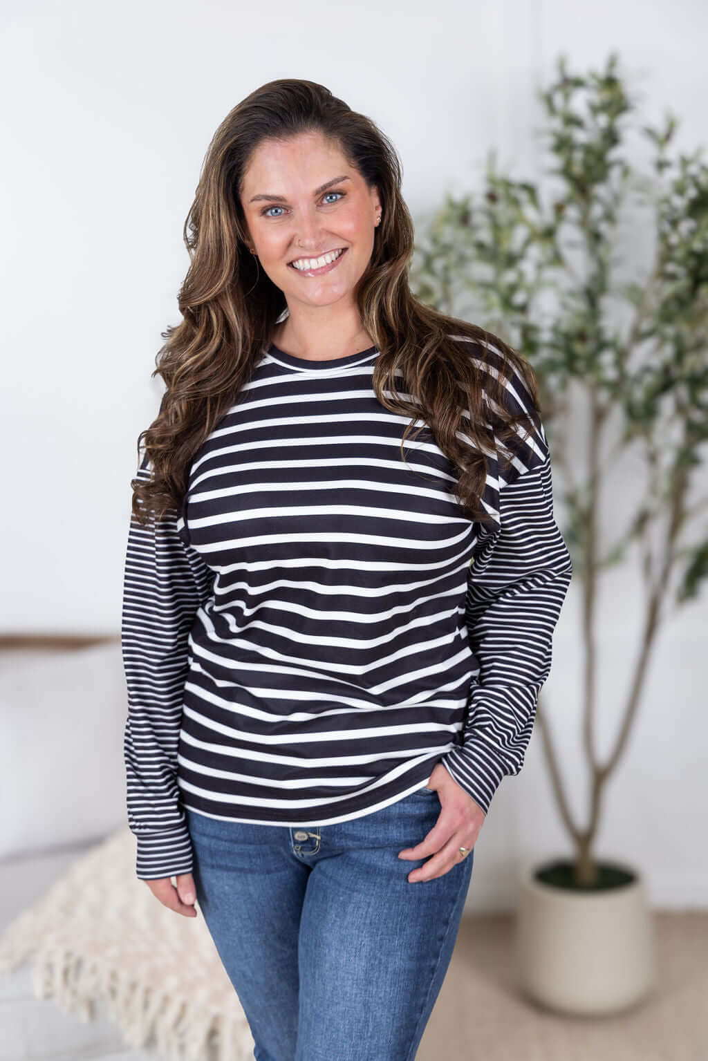 Model wearing black and white mixed stripe pullover top with relaxed fit and blue jeans