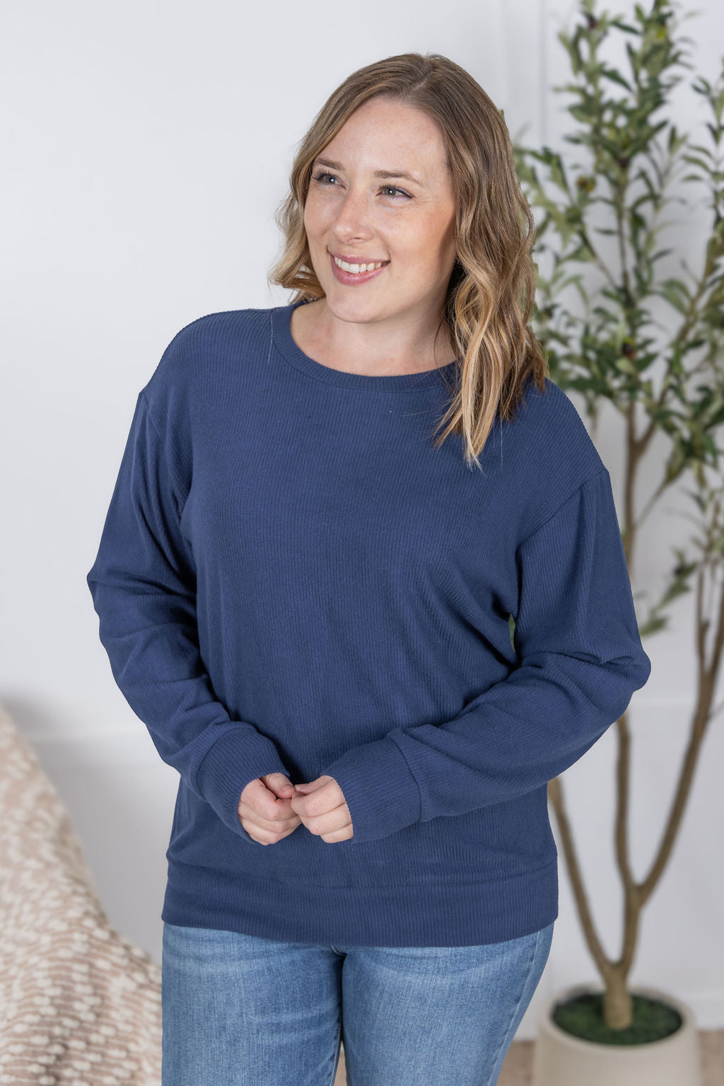Woman wearing a navy ribbed pullover top with long sleeves and light wash jeans