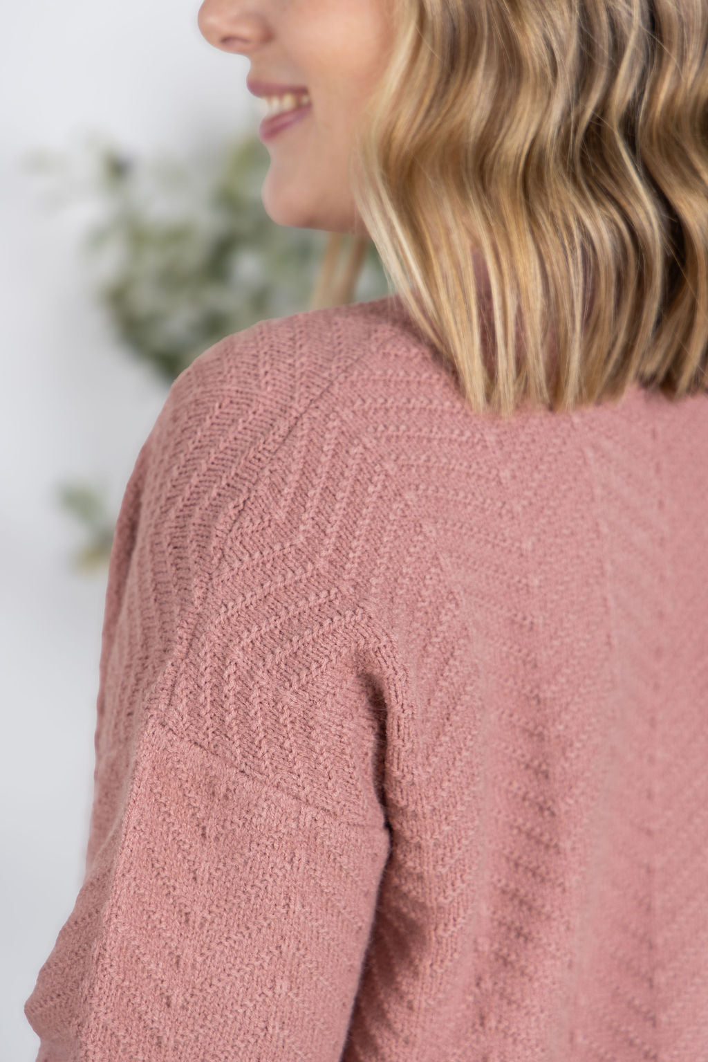 Close-up of a woman wearing the Chelsea Checkered Cardigan in brick red, featuring a v-neckline, button front, and ribbed cuffs and hem.