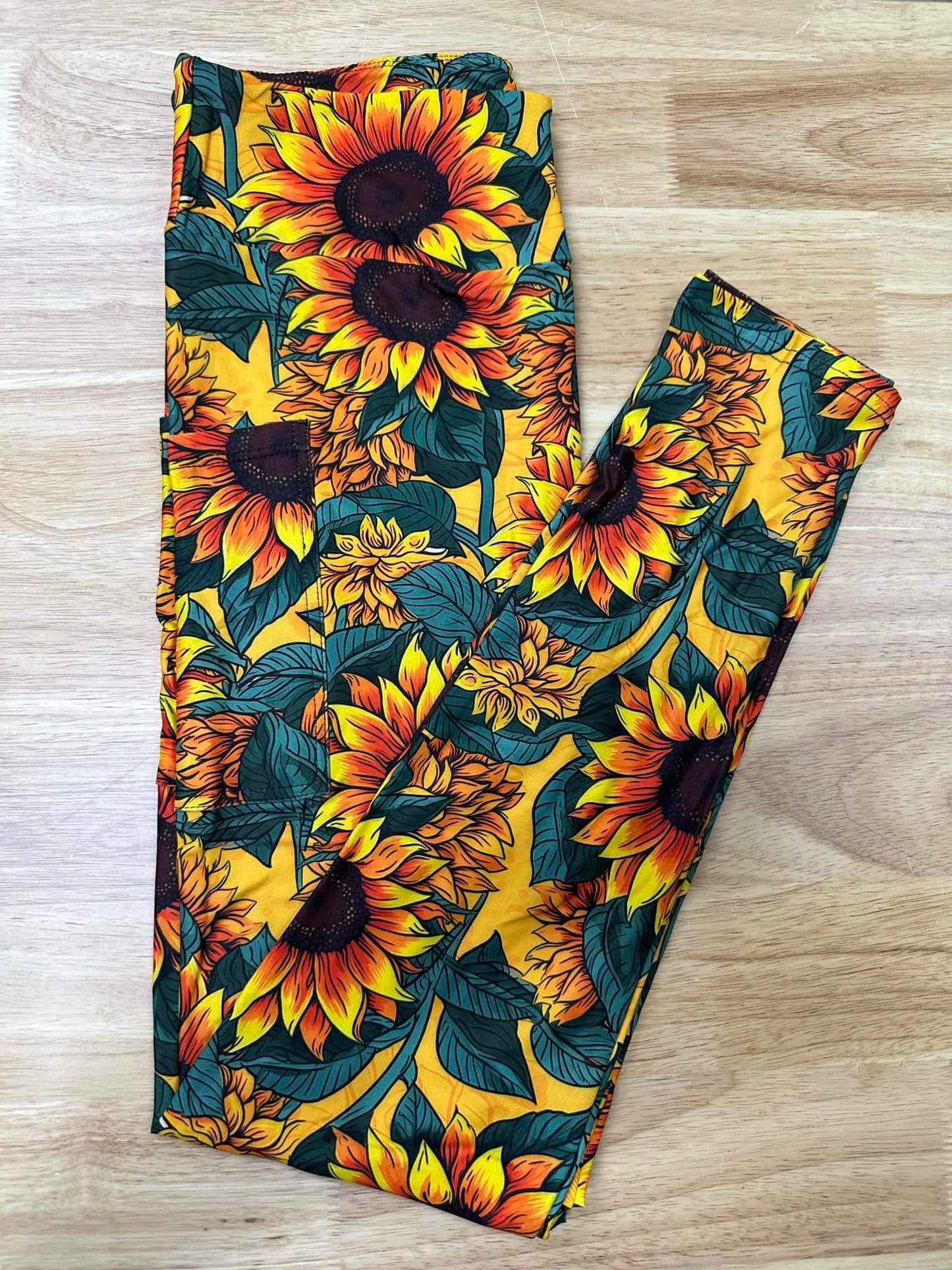 Folded leggings with vivid sunflower print in gold, orange, and green tones on a wooden background