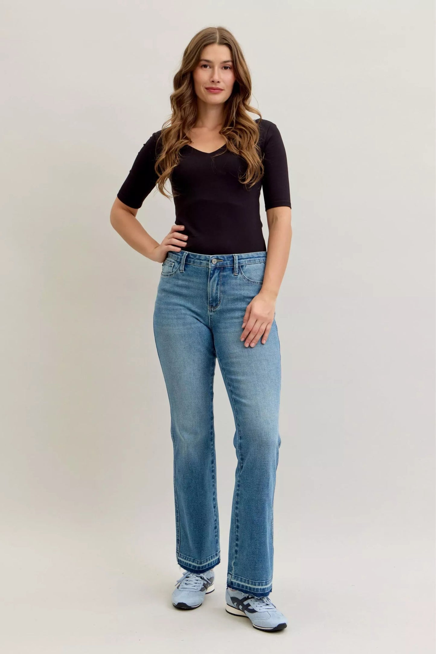 Woman wearing Callie faded medium wash mid rise bootcut jeans with tummy control panel and raw release hem