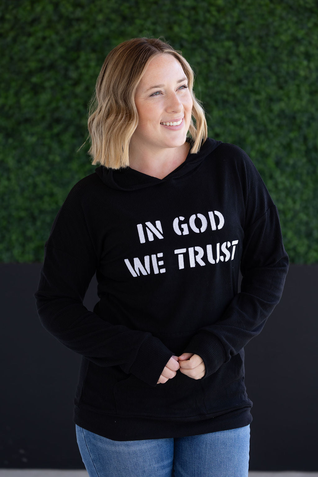 Corrine Embroidered Hoodie in black with “In God We Trust” design, kangaroo pocket, and cuff sleeves.