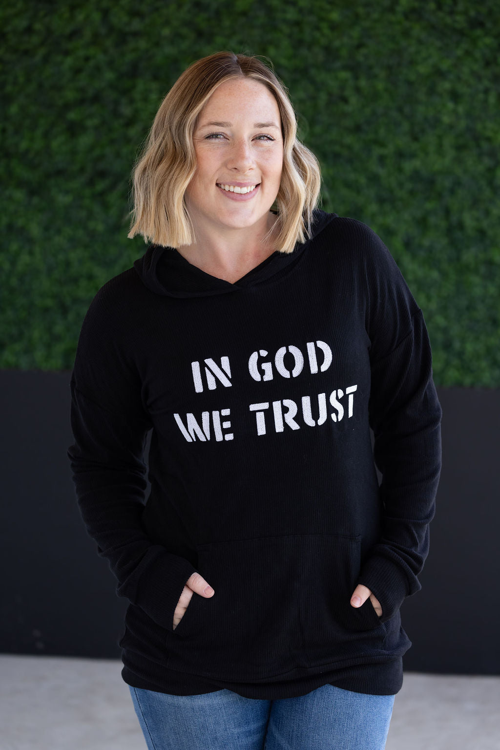 Corrine Embroidered Hoodie in black with “In God We Trust” design, kangaroo pocket, and cuff sleeves.