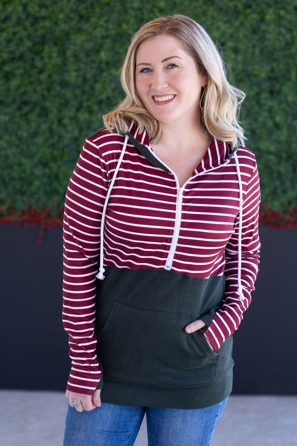 Woman wearing evergreen and burgundy striped half-zip hoodie with jeans
