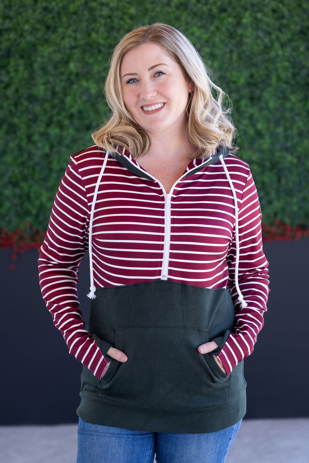 Woman wearing evergreen and burgundy striped half-zip hoodie with jeans