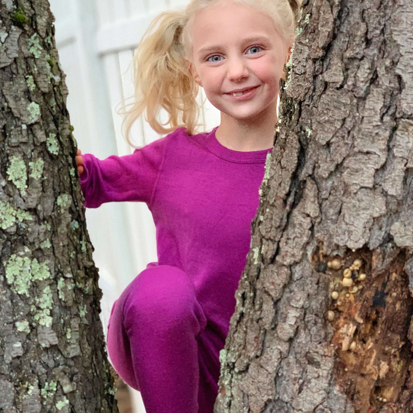 Child in a pink outfit peeking from behind a tree