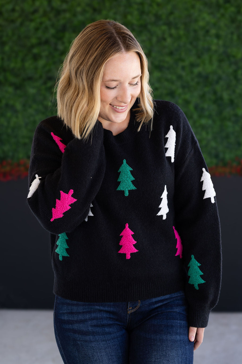 Black holiday sweater with white, green, and pink tree pattern, crew neckline, and cozy knit.
