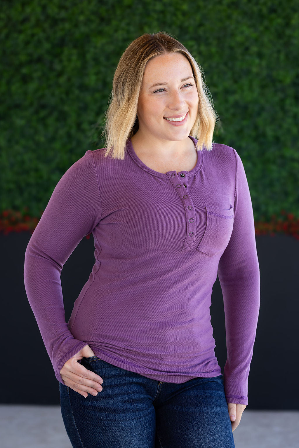 Woman wearing a purple long-sleeve shirt against a green wall.