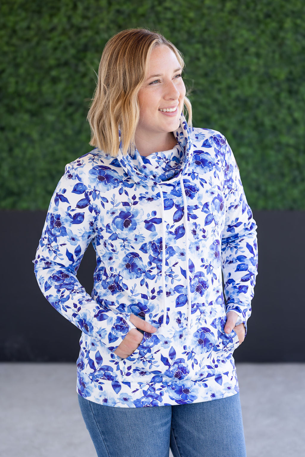 Woman wearing funnel neck sweatshirt with blue watercolor floral print all over, featuring cozy funnel neckline, long sleeves, and kangaroo pocket