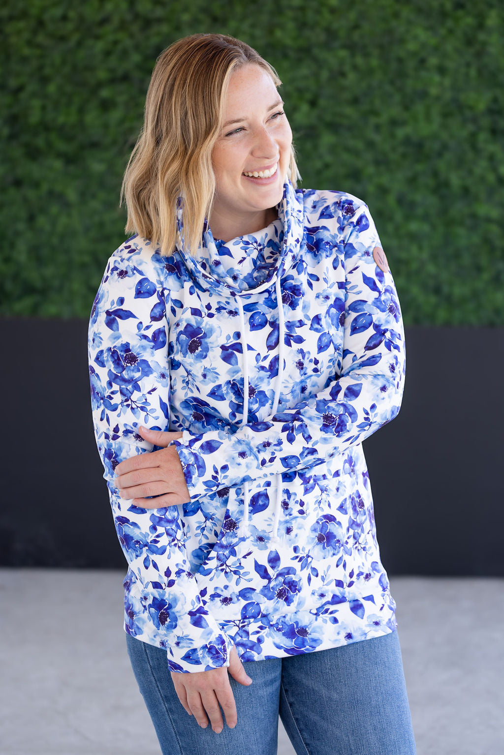 Woman wearing funnel neck sweatshirt with blue watercolor floral print all over, featuring cozy funnel neckline, long sleeves, and kangaroo pocket