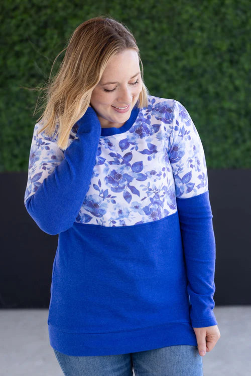 Woman wearing colorblock pullover with blue watercolor floral print on top and solid sapphire blue on bottom, featuring crew neckline and cuffed sleeves