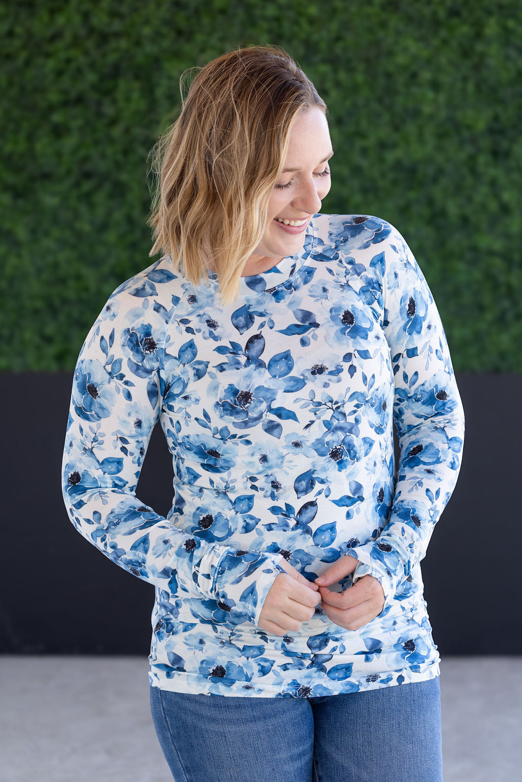 Woman wearing fitted long sleeve top with blue watercolor floral print all over, featuring high crew neckline and form-fitting silhouette